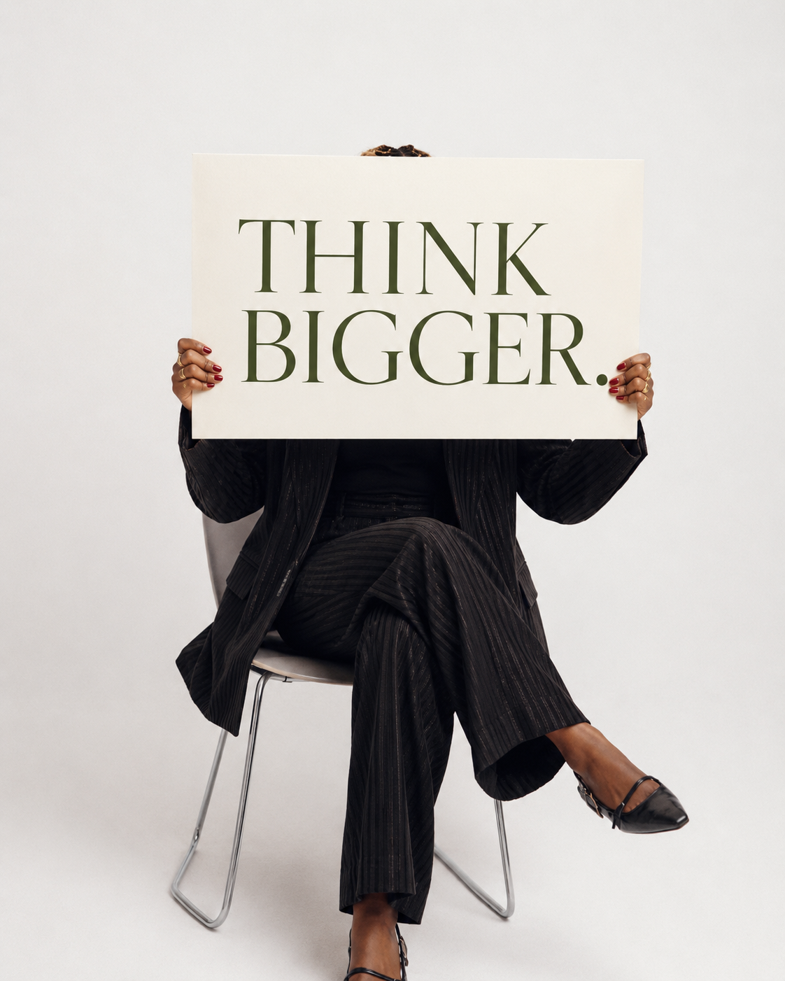 Shalom Kimani seated holding a Think Bigger sign